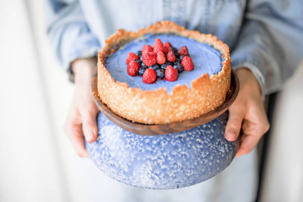 Woman holding berry cheesecake on a beautiful blue stand, close-up