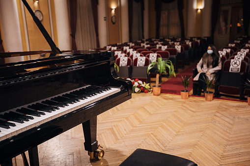 Grand Piano on stage in empty concert hall, one woman is sitting in audience.