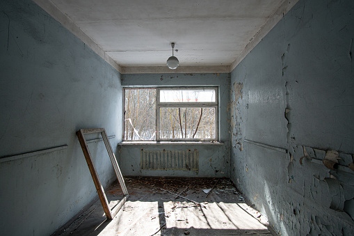Interior of an abandoned room with a broken window frame and peeling walls painted blue in the sunny day.