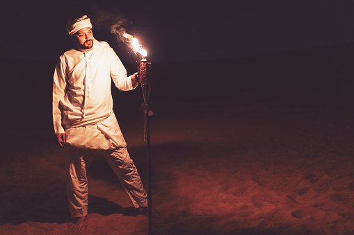 Arab man casually standing and setting up an oil lamp at a desert safari camp
