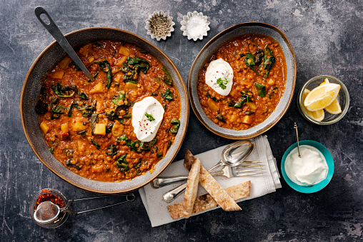 A thick vegetarian soup made with: onions, chilli, ginger, garlic, tinned tomatoes, potatoes, red lentils and wilted spinach, served with greek yoghurt, squeeze of lemon and toasted pitta bread. Overhead view, colour, horizontal with some copy space.