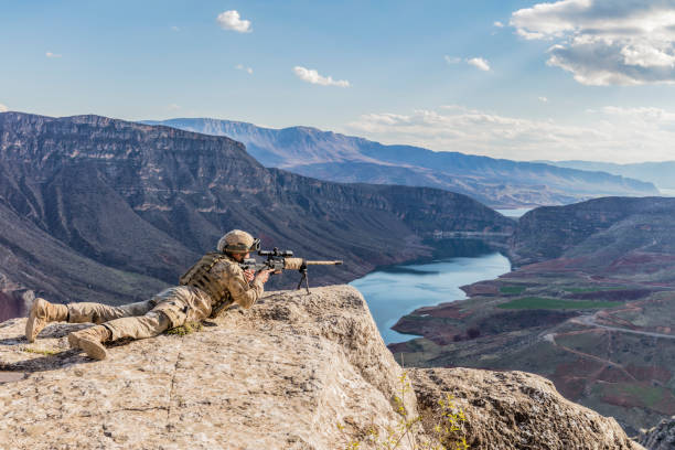 Army sniper aiming at his target on the top of cliff Army sniper aiming at his target on the top of cliff sniper stock pictures, royalty-free photos & images