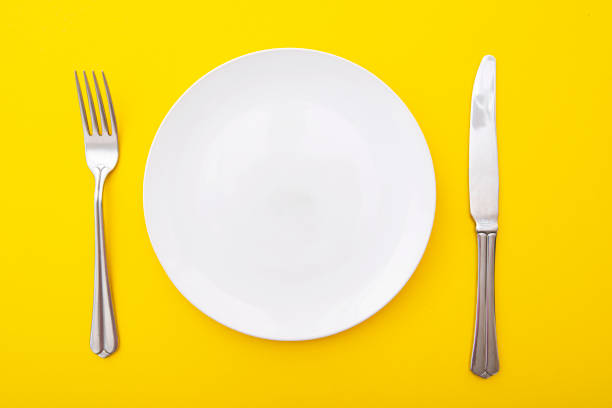istock Ceramic white plate with knife and fork on yellow surface, kitchen table, lay out, top view, space for text 1307975719