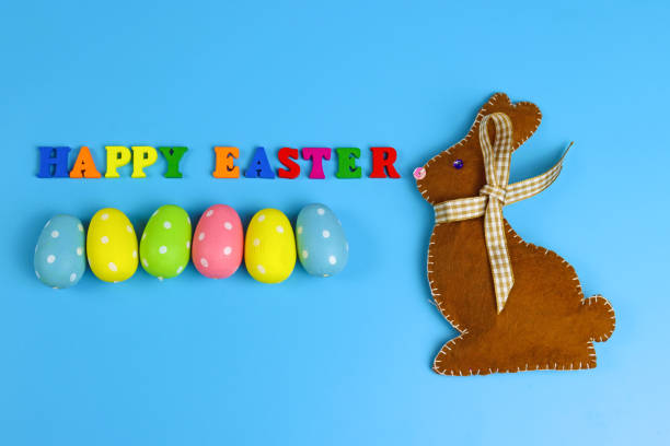 istock Inscription Happy Easter made of colored letters, painted eggs and felt rabbit on a blue background 1307978765