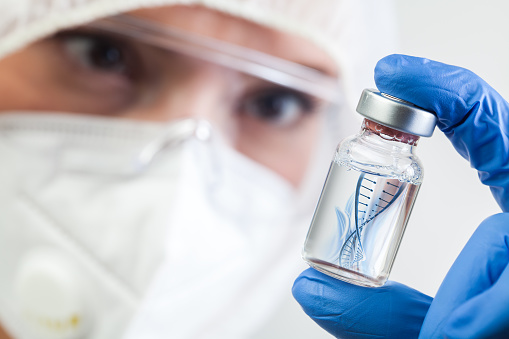 Microbióloga del NHS o biotecnológica de laboratorio sosteniendo frasco de vidrio con helice de ADN flotando en líquido photo