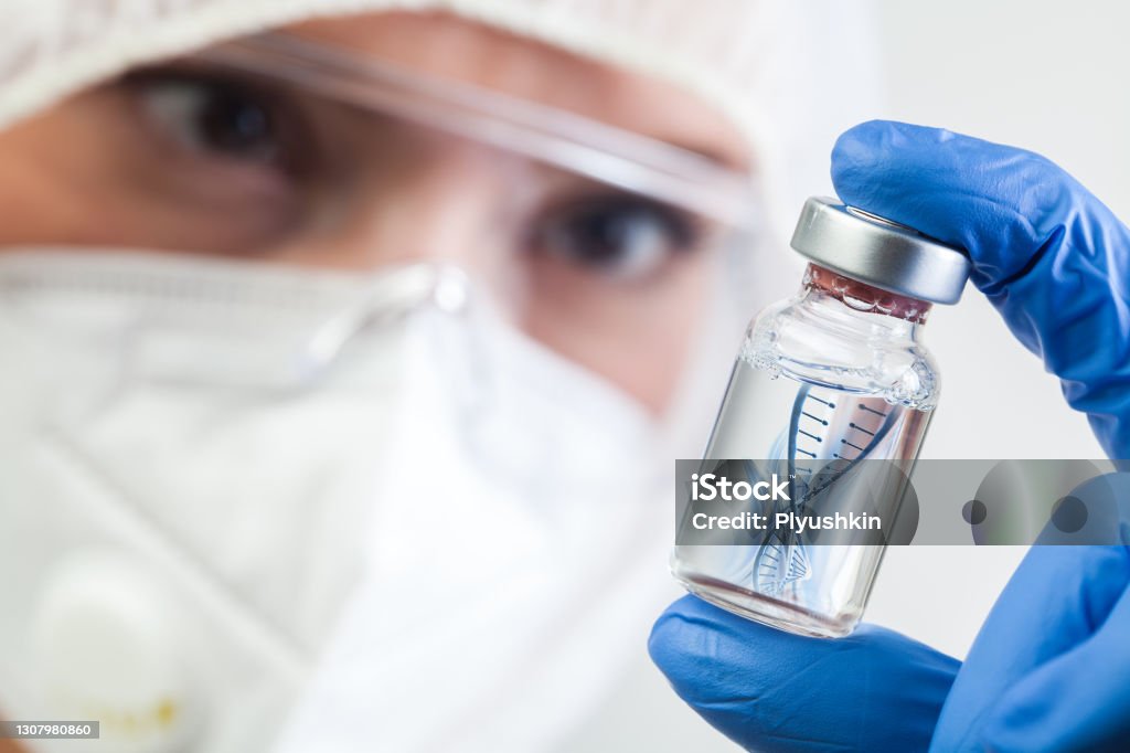 Female NHS microbiologist or lab biotechnician holding glass bottle vial with DNA helix strand floating in liquid Female NHS microbiologist or lab biotechnician holding glass bottle vial with DNA helix strand floating in liquid,Coronavirus new strain mutation,second variant found in UK,COVID-19 pandemic crisis DNA Stock Photo