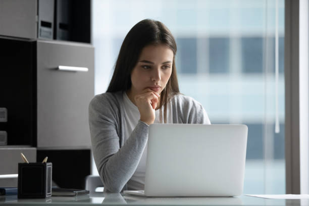 istock Pensive female sitting at office desk looking at laptop screen 1307981075