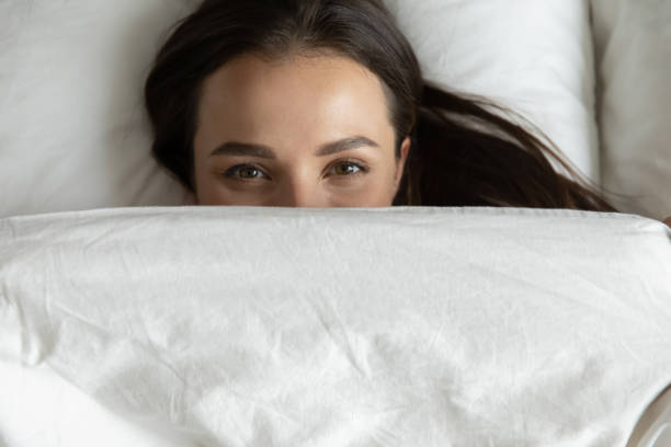 istock Joyful young female resting in bed covering face with blanket 1307981120