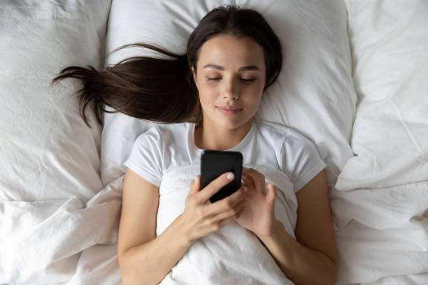 istock Smiling young female spending time in bed with mobile phone 1307981125