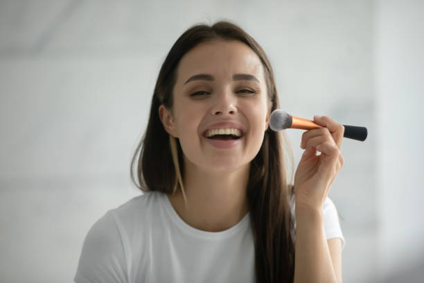 istock Laughing young female putting powder on face using makeup brush 1307981156