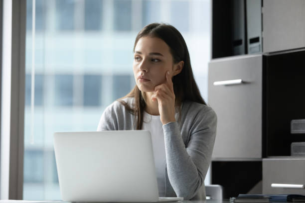 istock Thoughtful millennial female employee sitting at laptop distracted from work 1307981177