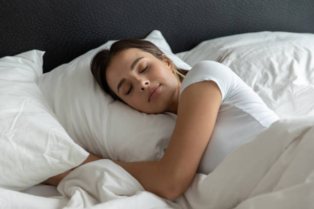 Relaxed young female sleeping in large cozy bed hugging pillow