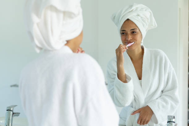 istock Mixed race woman wearing bathrobe and brushing teeth in bathroom 1307981488