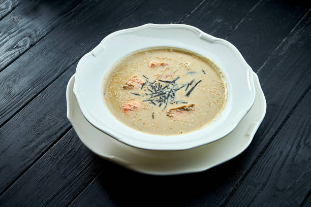 Appetizing coconut soup with salmon, nori and sesame seeds, served in a white plate on a dark wood background. Pan-Asian cuisine