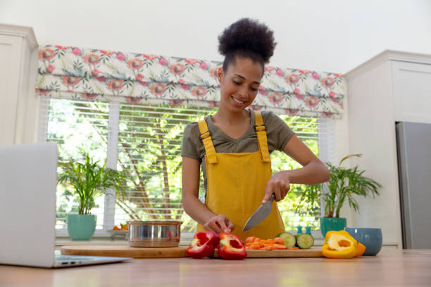 istock Mixed race woman cutting vegetables using laptop and smiling in a kitchen 1307988603