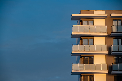 The building is a new block of flats, two-storeyed with glass balconies from the outside against the sunset sky