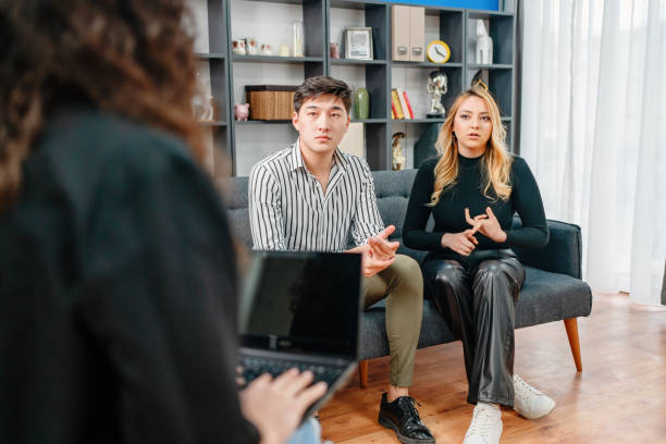 terapeuta familiar hablando con una pareja joven sentada en el sofá en la oficina - couple therapy alternative therapy relationship difficulties fotografías e imágenes de stock