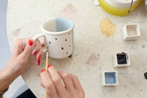 Women's hands apply a simple pattern to a ceramic teacup. Learning new skills, improving skills, hobbies.