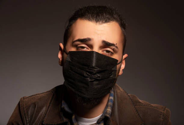 istock Sick man wearing protective mask in front of grey background looks towards camera. 1307993800