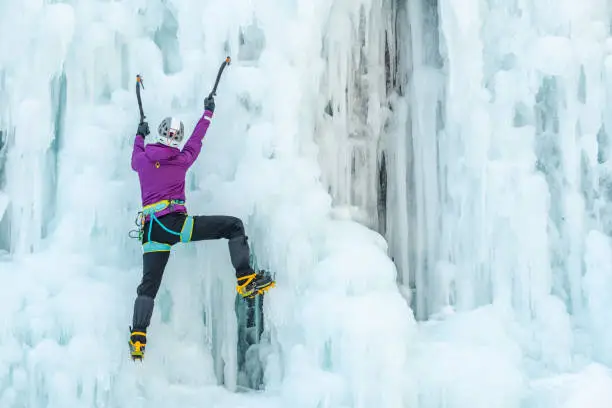 Woman with ice climbing axe hiking at a frozen waterfall