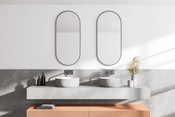 istock Comfortable two sinks with oval mirrors standing on marble countertop in modern bathroom with white walls. 1307994734