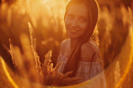 Beautiful carefree woman in fields being happy outdoors. Outdoor atmospheric lifestyle photo of young beautiful lady. Brown hair and eyes. Warm autumn. Warm spring