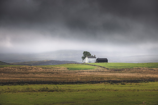 Lone, secluded farmhouse on a stormy, moody English countryside rural landscape in the North Pennines AONB, England UK.