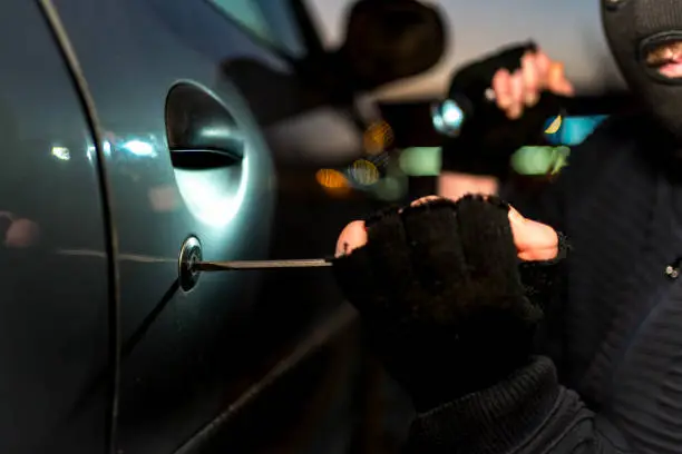 Masked man using a screwdriver to brake into a car at night