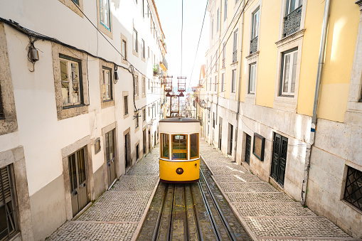Trams in Lisbon city. Famous retro yellow funicular tram on narrow streets of Lisbon old town on a sunny summer day. Tourist attraction. High quality photo