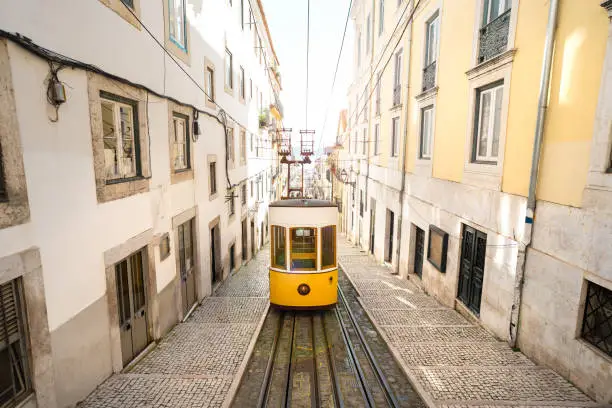 Photo of Trams in Lisbon city. Famous retro yellow funicular tram on narrow streets of Lisbon old town on a sunny summer day. Tourist attraction