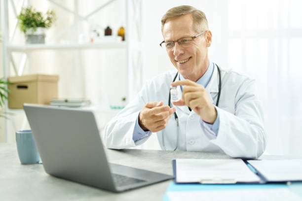 istock Cheerful doctor holding coronavirus vaccine and using laptop 1308004271