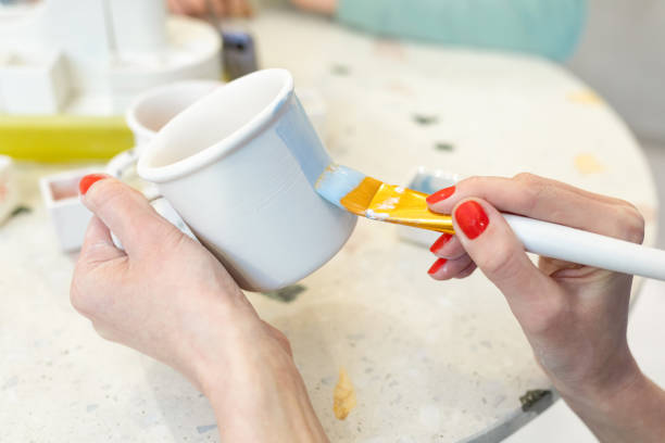 istock Women's hands with a bright red manicure paint a clay mug in blue. Ceramic art. Selective focus 1308008127