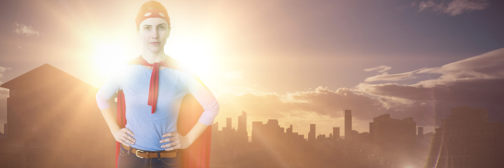 Woman pretending to be superhero against picture of city by sunrise