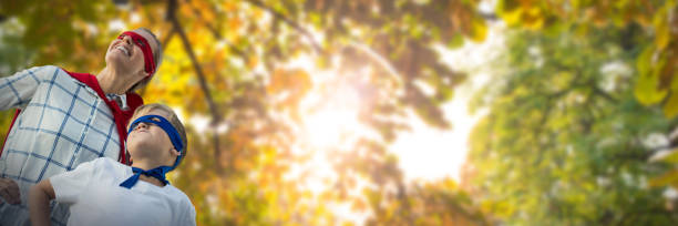Composite image of mother and son pretending to be superhero Mother and son pretending to be superhero against low angle view of back lit trees superhero environment women green color stock pictures, royalty-free photos & images