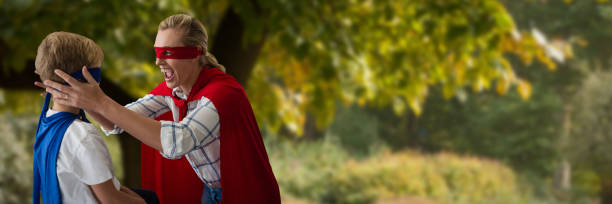 Composite image of mother and son pretending to be superhero Mother and son pretending to be superhero against tree by footpath superhero environment women green color stock pictures, royalty-free photos & images