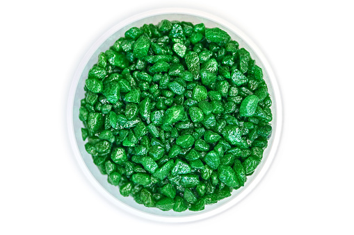 Emerald gemstone fake in bowl. Green glitter stones for garden decoration, flat lay, isolated white top view background.