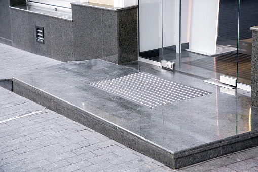marble gray porch step with a foot mat at the entrance to the central door made of tempered glass on floor iron hinges modern architecture with a stone apron of the building facade, nobody.