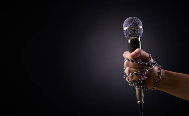 istock World press freedom day concept. Hand holding a microphone with chain on dark background, symbol of press freedom of speech freedom. 1308020394