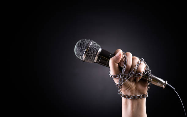 World press freedom day concept. Hand holding a microphone with chain on dark background, symbol of press freedom of speech freedom. World press freedom day concept. Hand holding a microphone with chain on dark background, symbol of press freedom of speech freedom. censorship stock pictures, royalty-free photos & images