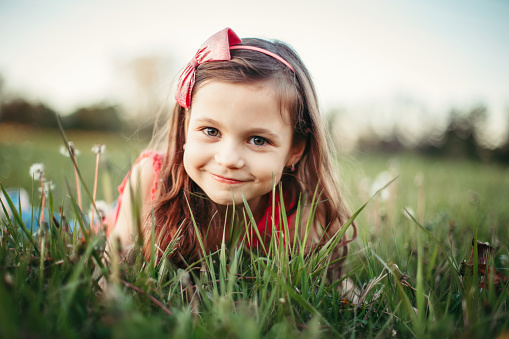 Cute adorable Caucasian girl among dandelions flowers. Child lying in grass on meadow. Outdoor fun summer seasonal children activity. Kid having fun outside. Happy childhood lifestyle.