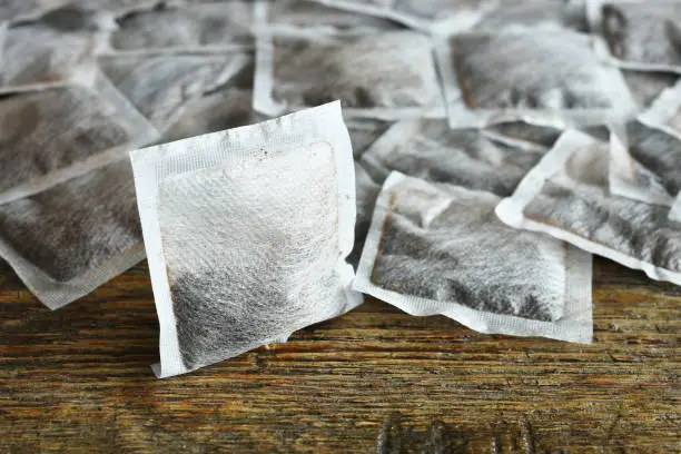 A close up image of several square tea bags on an old vintage table top.