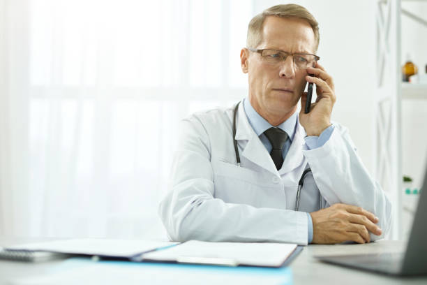 istock Serious doctor talking on mobile phone and using laptop at work 1308034746