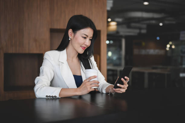 istock Successful businesswoman holding coffee cup and using smart phone in modern workplace. 1308038096