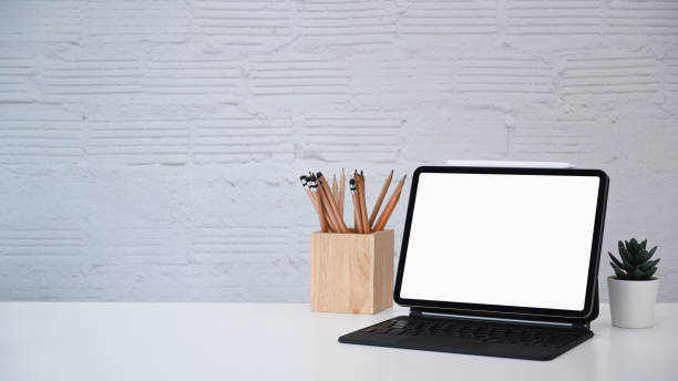 istock Designer workplace with computer tablet, plant, cactus and pencils holder on white desk. 1308038740