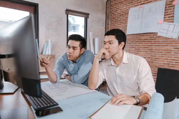 Photo of engineers and architect reading a building and  drawing outlay construction plan as guide for builders with details on computer. Engineer design and writing blueprint.