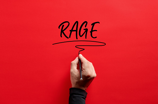 Male hand writing the word rage on red background. Rage and anger concept.
