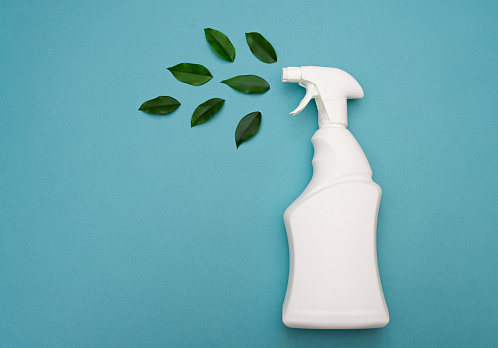 Empty white bottle mockup for cleaning and tidying up. Ecological object. Environmentally friendly cleaning products. The concept of natural ecological cleaning products. White bottle with spray bottle and green leaves on a blue background, copy space. mockup