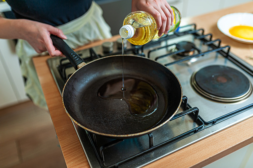 Close-Up Photo of a Woman who is Preparing to Fry a Meat in a Frying Pan While Pouring an Oil into a Cooking Pan in the Kitchen.
