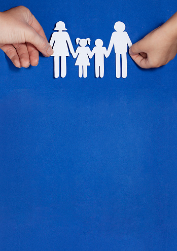 A child and a mother hold hands with a family cut out of paper. Blue paper background. Family home, adoption, foster family, autism support, happy family