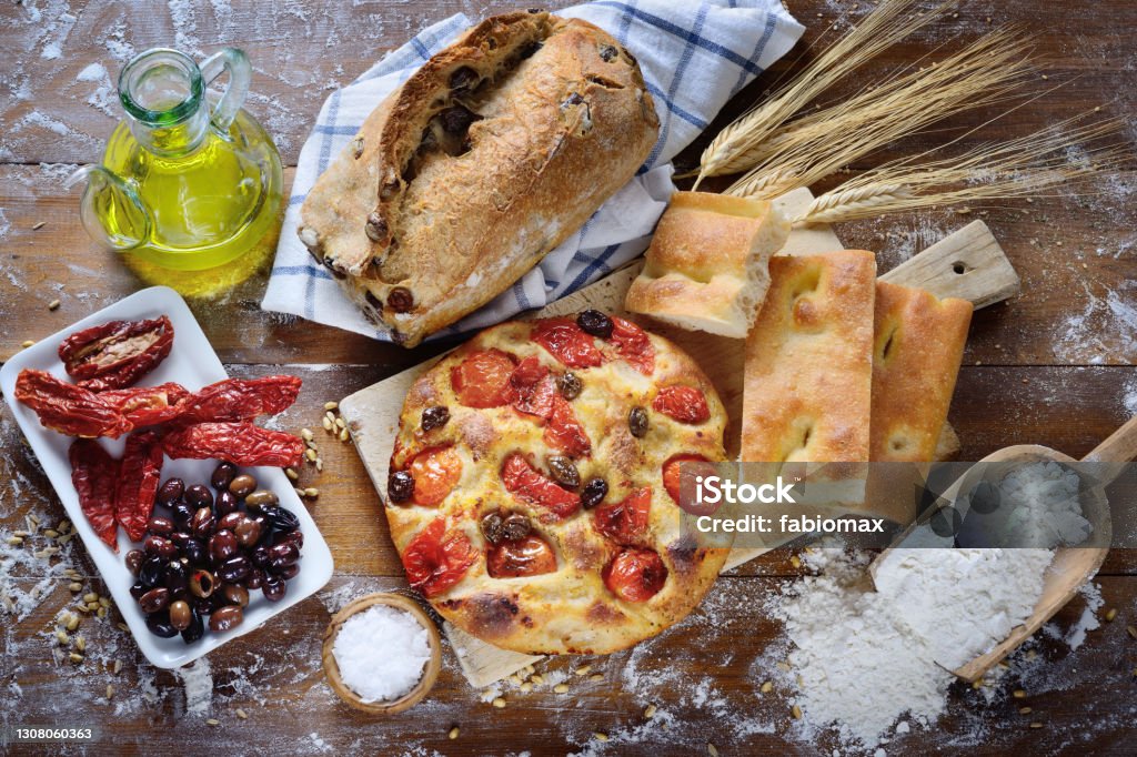 Focaccia with cherry tomatoes and olives, olive bread, white focaccia, dried tomatoes and olives, top view. Focaccia from Bari and other baked goods on rustic wooden table. Puglia Stock Photo